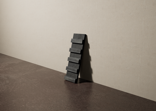 a 4"x12.5" bespoke dimensional concrete tile with five evenly spaced tiers leans against a textured, plaster wall on an unfinished concrete floor